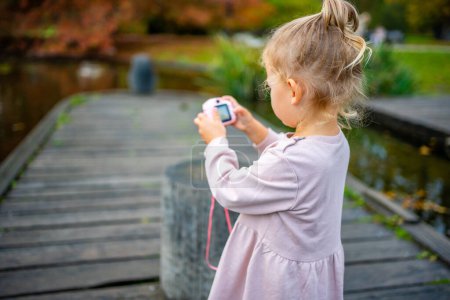 Petite fille prenant des photos avec appareil photo numérique rose pour enfants dans le parc d'été. Photo de haute qualité