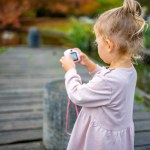 Toddler Girl Taking Pictures with Pink Digital Childrens Camera in the Summer Park . High quality photo