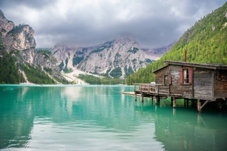 Photo for Wooden house on Braies lake surrounded by pine forests and the rocky ranges of the Dolomites in cloudy day, Italy. High quality photo - Royalty Free Image