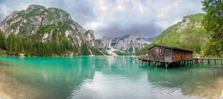 Photo for Dolomites, Italy - August 4, 2023: Wooden house on Braies lake surrounded by pine forests and the rocky ranges of the Dolomites in cloudy day, Italy. High quality photo - Royalty Free Image