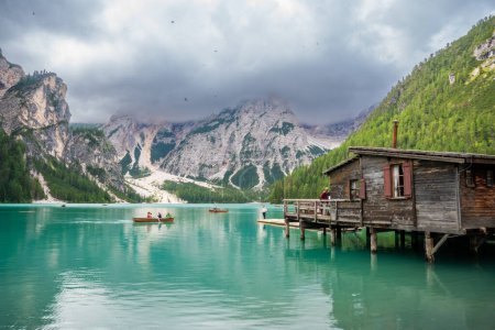 Photo for Dolomites, Italy - August 4, 2023: Wooden house on Braies lake surrounded by pine forests and the rocky ranges of the Dolomites in cloudy day, Italy. High quality photo - Royalty Free Image