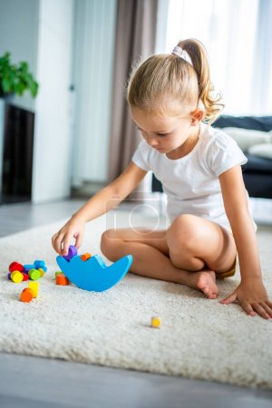Foto de Niña jugando con el juguete de equilibrio de madera en el suelo en la sala de estar en casa. Foto de alta calidad - Imagen libre de derechos