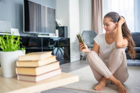 Una mujer joven está tratando de leer un libro, pero está constantemente distraída por su teléfono inteligente y las redes sociales. Foto de alta calidad