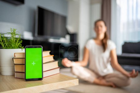 Concepto de desintoxicación digital. Smartphone con pantalla de croma verde y mujer meditando en segundo plano. Foto de alta calidad