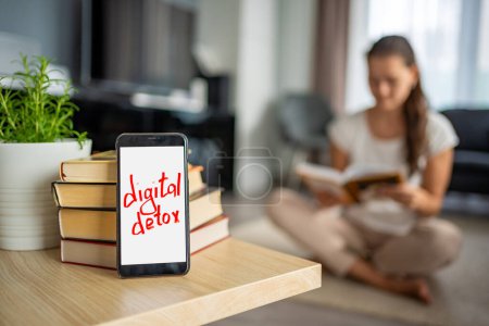 Digitales Detox-Konzept Foto. Smartphone mit dem Text Digital Detox und Frau liest Buch im Hintergrund. Hochwertiges Foto