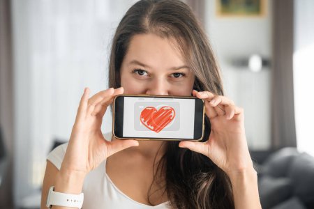 Foto de Concepto del Día Mundial de la Salud. Mujer joven mostrando ilustración del corazón en su smartphone, ilustrando la importancia de la conciencia de la salud cardiovascular en la observación internacional de la salud. - Imagen libre de derechos