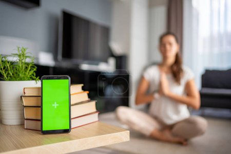 Concepto de desintoxicación digital. Smartphone con pantalla de croma verde y mujer meditando en el fondo. Foto de alta calidad