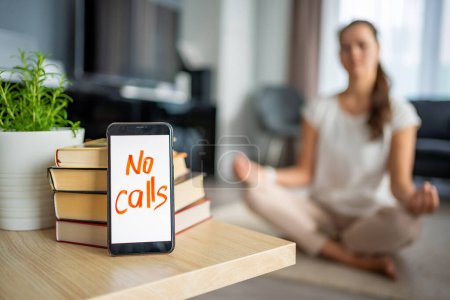 Digital detox concept. In the foreground is a smartphone with the text No Calls and woman meditating in the background. High quality photo