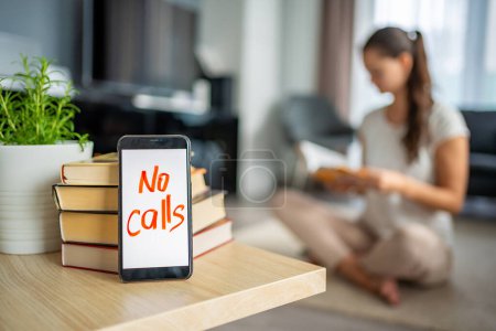 Digital detox concept photo. Smartphone with the text No Calls and woman reading book in the background. High quality photo