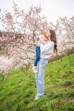 Young woman with little daughter in a blooming pink and white garden Petrin in Prague, spring time in Europe. High quality photo