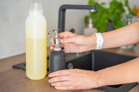 Eine Frau plant, Seife oder Waschmittel aus recycelten Verpackungen in eine Mehrwegflasche zu gießen. Umweltfreundliches Lifestylekonzept. Hochwertiges Foto