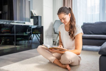 Young woman reads book sitting on the floor in the living room. High quality photo