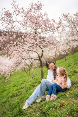 Young woman with little daughter in a blooming pink and white garden Petrin in Prague, spring time in Europe. High quality photo