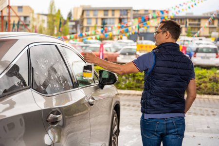 Hombre joven aplica líquido para limpiar las ventanas del coche en el auto-servicio de lavado de coches.