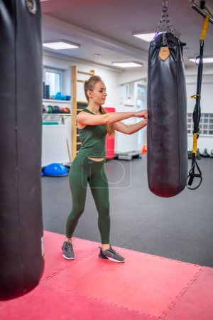 Young woman stands next to a black boxing pear to let off steam in gym. High quality photo