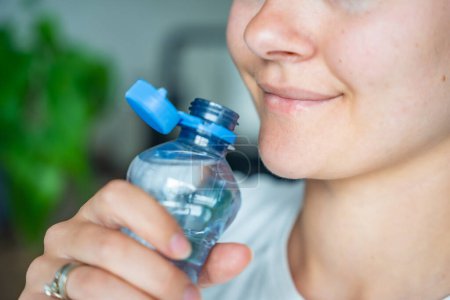 Young woman drinking from a bottle with stationary plastic cap. The new design means the cap remains attached to the bottle after opening, making the entire package easier to collect and recycle. 
