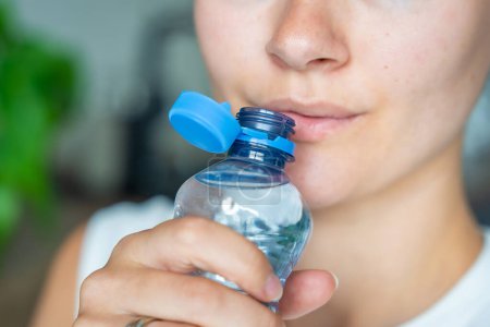 Mujer joven bebiendo de una botella con tapa de plástico fija. El nuevo diseño significa que la tapa permanece unida a la botella después de la apertura, lo que hace que todo el paquete sea más fácil de recoger y reciclar.. 