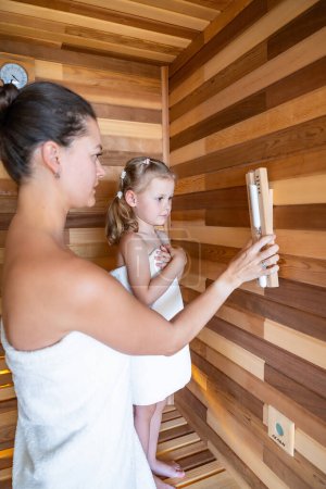 Mom and daughter control the time spent in the sauna enjoying time together. Girly pastime. High quality photo