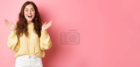 Photo for Happy beautiful girl gasping amazed, clap hands and smiling, looking surprised, receive great news, being praised, standing against pink background. - Royalty Free Image