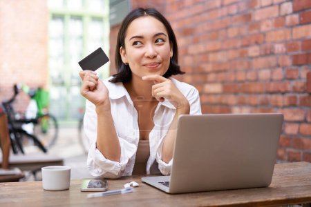 Photo for Stylish young asian woman doing shopping online, sitting with credit card and laptop, buying in internet and paying contactless, dealing with bills. - Royalty Free Image