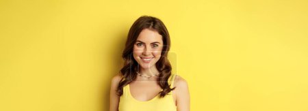 Foto de Primer plano retrato de mujer morena con sonrisa blanca sana, mirando feliz y confiado, posando sobre fondo amarillo. - Imagen libre de derechos