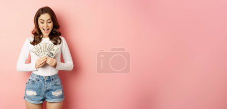 Foto de Loans and microcredit. Smiling beautiful girl showing money, cash in hands and looking enthusiastic, standing over pink background. - Imagen libre de derechos