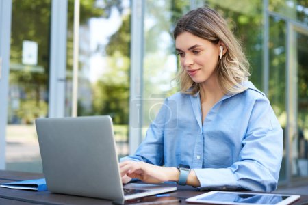 Photo for Portrait of corporate woman working outside office on remote, sitting with laptop, wireless earphones, attend online video conference. - Royalty Free Image