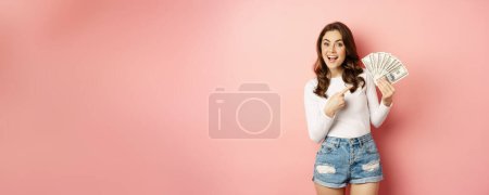 Foto de Attractive young woman holding money, cash in hands, concept of loans, microcredit and shopping, standing over pink background. Copy space - Imagen libre de derechos