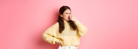 Photo for It stinks. Disgusted glamour girl shuts her nose from awful smell, look accusingly at camera, something reek bad, standing over pink background. Copy space - Royalty Free Image