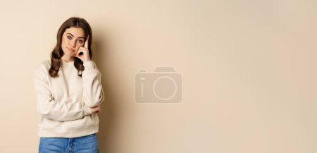 Photo for Annoyed woman, roll eyes and looking unamused, bothered and bored, standing over beige background. - Royalty Free Image