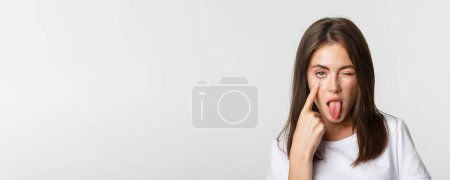 Foto de Primer plano de chica joven atractiva tonta mostrando la lengua y tirando del párpado, mirándote. - Imagen libre de derechos