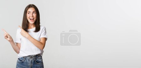 Foto de Atractiva chica morena sonriente señalando los dedos esquina superior izquierda, mostrando logo. - Imagen libre de derechos