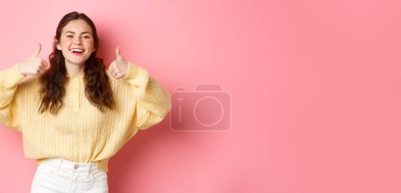 Foto de Muy bien, bien hecho. Sonriendo chica de apoyo, riendo y mostrando los pulgares hacia arriba en la aprobación, como la idea impresionante, alabanza, de pie sobre el fondo rosa. - Imagen libre de derechos