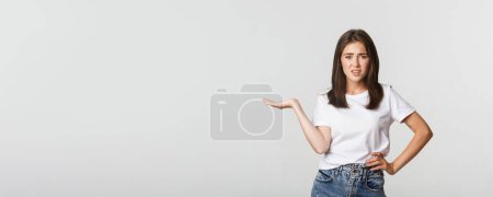 Photo for Skeptical and unamused young bothered girl shrugging, raise one hand displeased. - Royalty Free Image