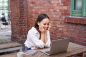 Happy asian girl watching video on laptop, doing homework outdoor in coworking space, smiling and working, drinking coffee. tote bag #621634760