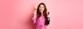 Celebration and holidays concept. Beautiful woman saying toast, raising glass of champagne and holding bottle, having fun at party, standing against pink background. Poster #621846908