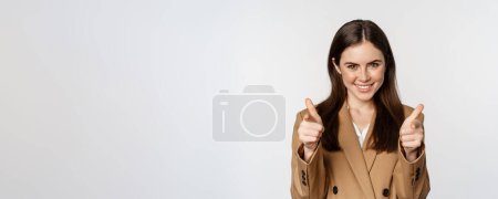 Téléchargez les photos : Enthusiastic businesswoman, corporate woman showing thumbs up and smiling, complimenting, recommending company, standing over white background. - en image libre de droit
