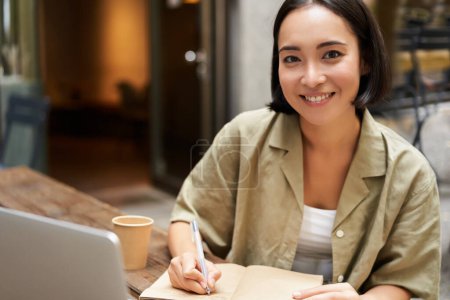 Foto de Retrato de una joven mujer asiática trabajando en el portátil, tomando notas, escribiendo mientras asistía a la lección en línea, reunión de trabajo. - Imagen libre de derechos