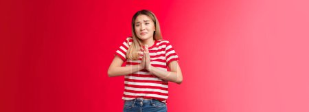 Photo for Gloomy upset girl in need begging mercy, asking apology feel guilty sad. Clingy cute daughter frowning grimacing unhappy sorrow hold hands pray pleading borrow car, supplicating red background. - Royalty Free Image