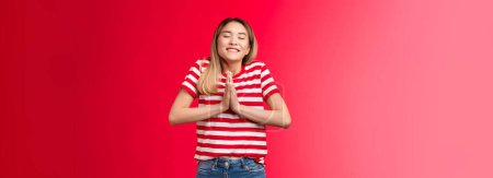 Photo for Dreamy enthusiastic attractive tender modern asian blond girl praying believe dreams come true, ask Lord favour, supplicating, hold palms together make wish stand red background. Copy space - Royalty Free Image