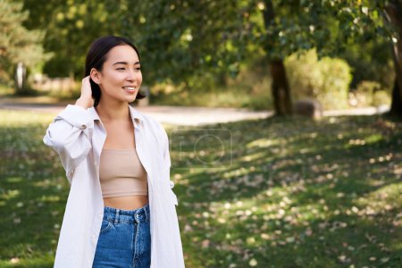 Photo for Beautiful young asian girl smiling, laughing and walking along park, enjoying summer sunny day. People and lifestyle concept - Royalty Free Image