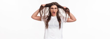 Photo for Waist-up portrait of bothered and annoyed, angry pissed-off young girlfriend losing temper, pulling hair from head and screaming being furious and outraged, white background. - Royalty Free Image
