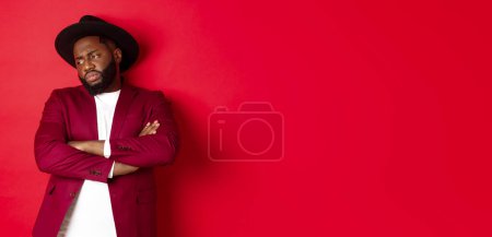 Photo for Reluctant and upset african american man looking away, cross arms on chest offended, standing distressed against red background. - Royalty Free Image