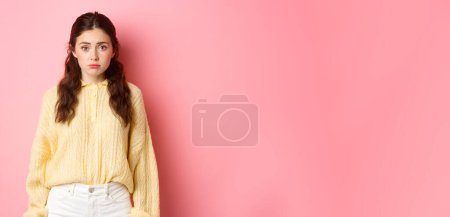 Téléchargez les photos : Triste femme mignonne regardant innocent et stupide à la caméra, debout sur fond rose. Espace de copie - en image libre de droit