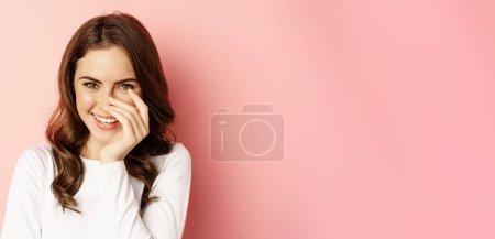 Foto de Primer plano retrato de mujer morena coqueta, riendo y sonriendo, mirando hacia abajo coqueta, de pie sobre fondo rosa. Copiar espacio - Imagen libre de derechos
