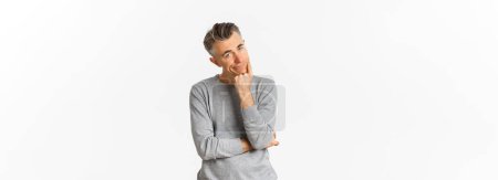 Photo for Portrait of bored and unamused middle-aged man in grey sweater, leaning on hand and looking at camera reluctant, standing sad over white background. - Royalty Free Image