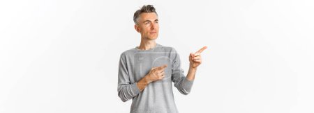 Photo for Image of thoughful handsome man, making decision, pointing and looking left at something interesting, showing logo over white background. - Royalty Free Image