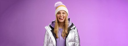 Photo for Lifestyle. Cheeky carefree delighted charming blond girl having fun feel amused positive show tongue smiling broadly wearing winter silver glittering jacket stylish hat enjoying awesome ski vacation. - Royalty Free Image