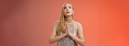 Photo for Hopeful worried concerned faithful blond woman in silver dress praying talking god wishing family okay press palms together supplicating nervously begging, standing red background stylish dress. - Royalty Free Image