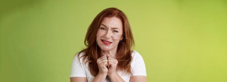 Photo for Silly touched tender redhead charmed middle-aged woman sighing gladly gaze admiration delighted press hands together heartwarmed fascinated look grateful lovely camera green background. - Royalty Free Image